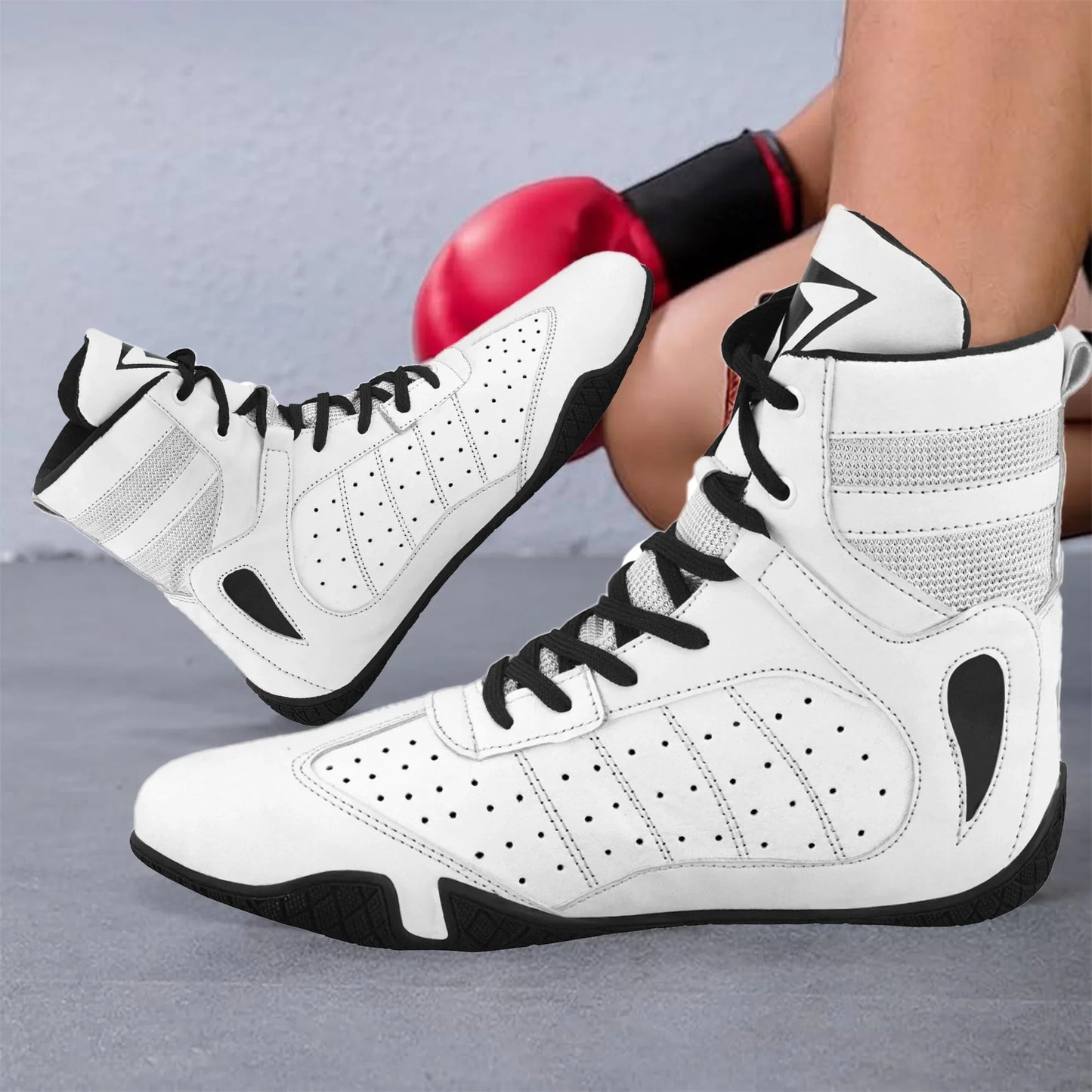 White high-top boxing shoes with black laces worn by athlete on gym floor, red boxing glove nearby