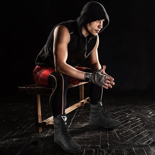 Man in boxing gear wearing black breathable boxing shoes, sitting on bench in gym