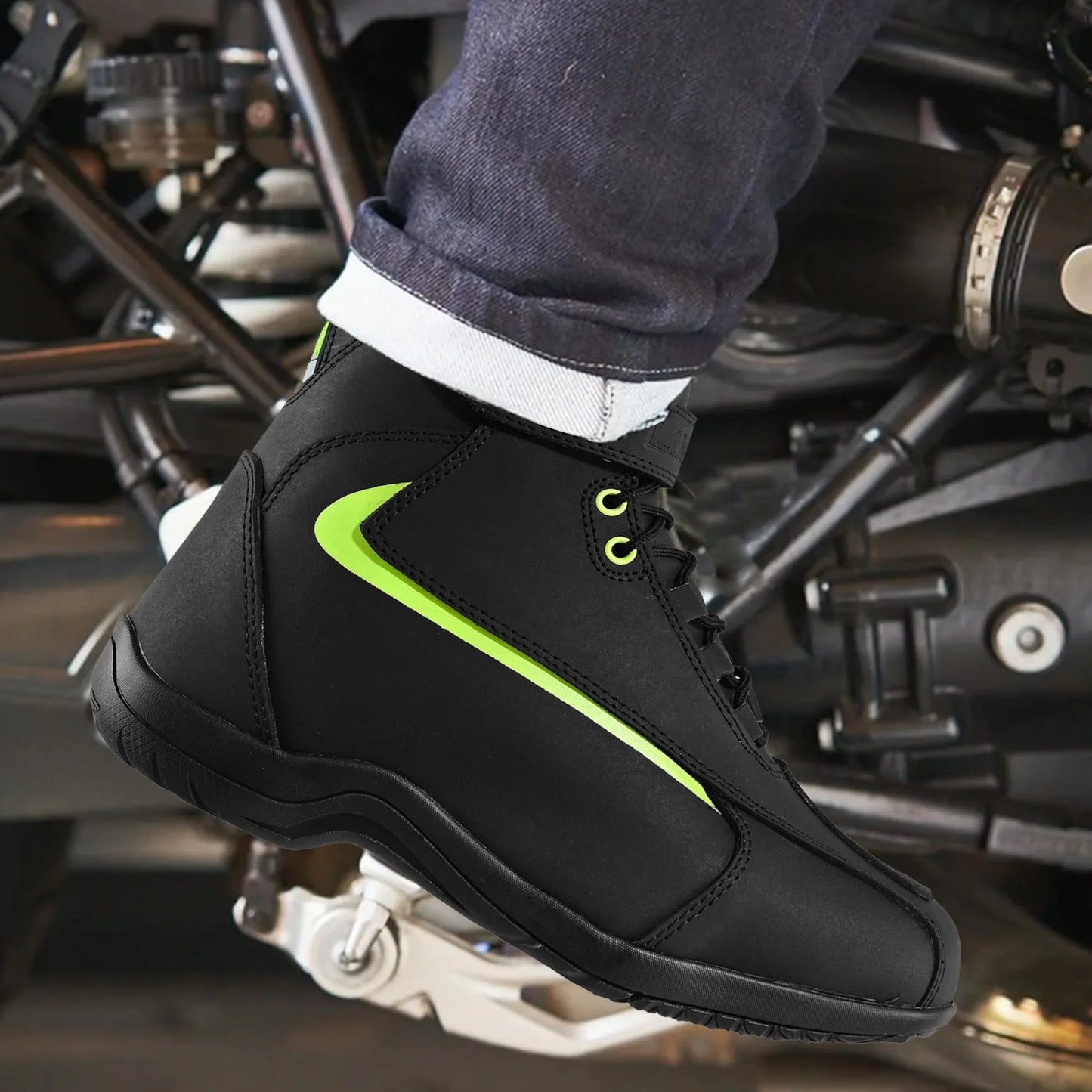 Black motorcycle riding shoe with neon green accents on a foot resting on a motorbike footpeg