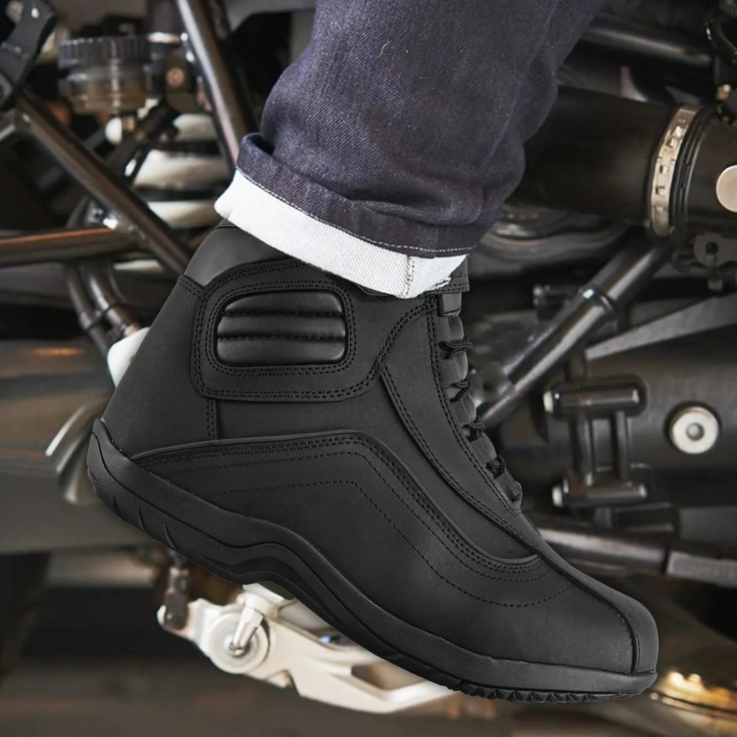 Black motorcycle riding boot on foot with jeans, positioned on motorcycle footpeg.