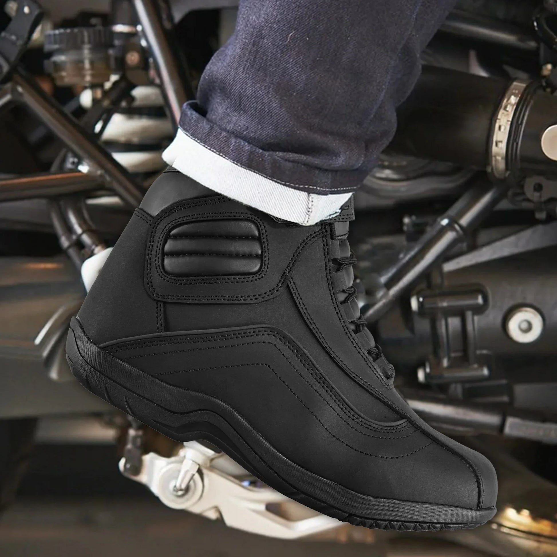 Black motorcycle riding boot on foot with jeans, positioned on motorcycle footpeg.